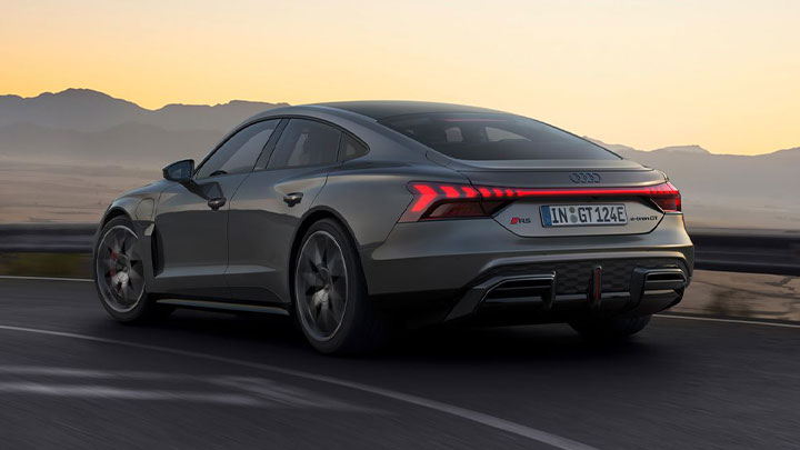 Rear quarter shot of a grey Audi RS e-tron GT driving down a road at sunset