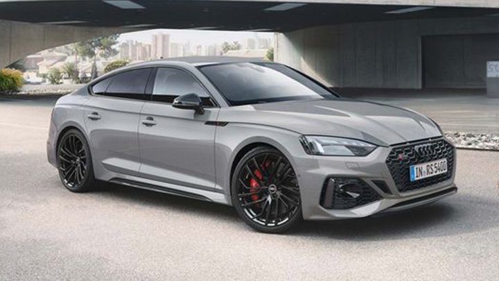 Side of grey Audi RS5 Sportback parked parked under a bridge with a large city in the background