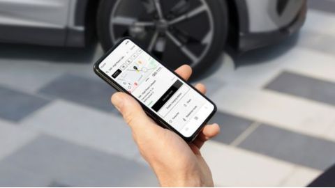 Man holding a smartphone with MyAudi app open in front of a silver Audi car