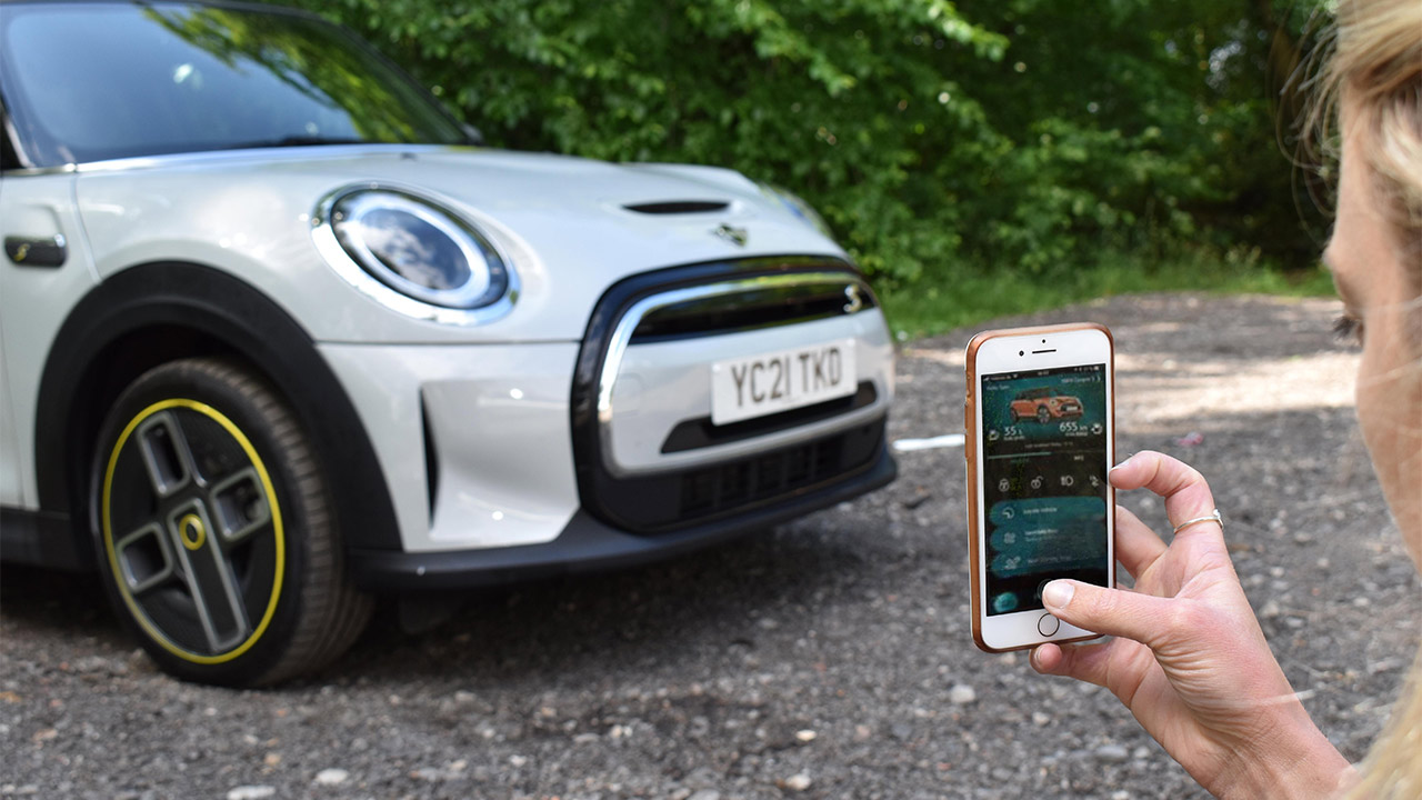 Woman using MINI Connected smartphone app, MINI Electric parked in background