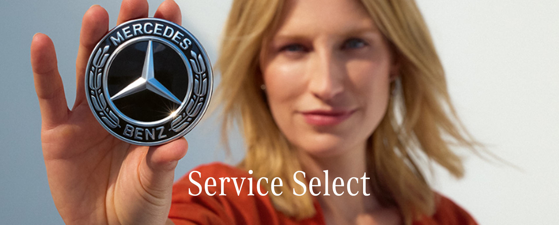 Blonde woman holding a Mercedes-Benz badge to the camera.